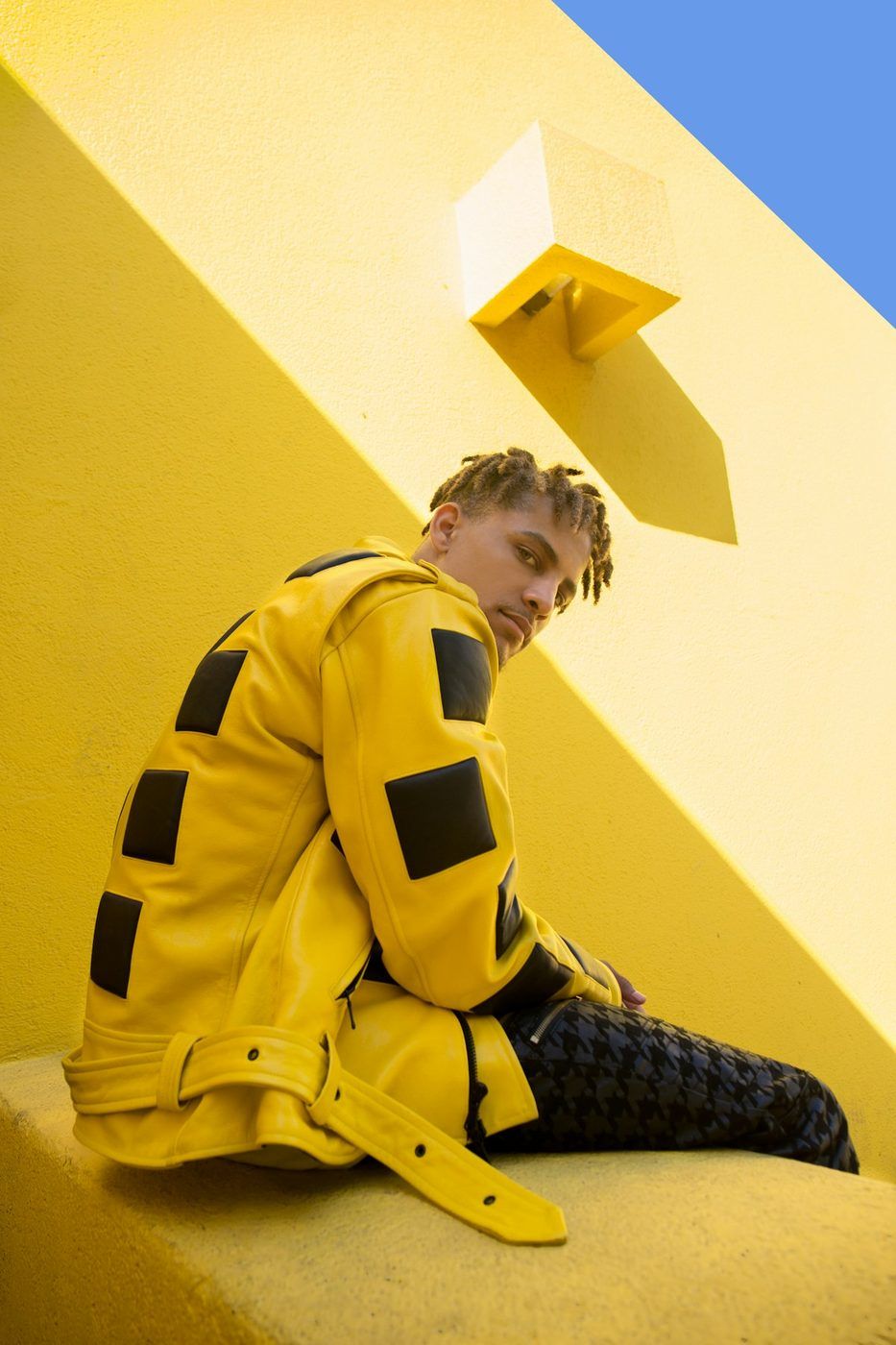 Model in a yellow jacket against a yellow wall in hard light